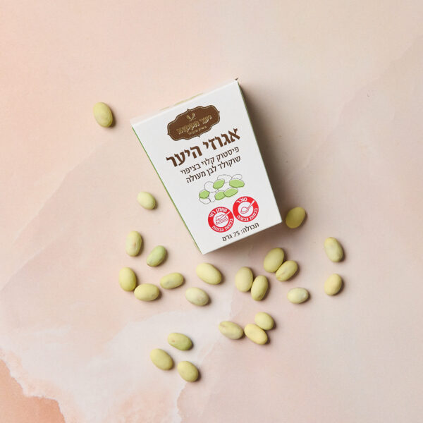 קופסה עם הכיתוב "IMG_2074" בעברית ועיצובים ירוקים מונחת על משטח שיש ורוד, מוקפת בסוכריות פיסטוק או שוקולד לבן בצורת אליפסה.