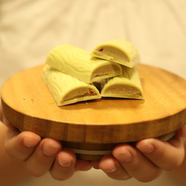 אדם מחזיק צלחת עץ עגולה ובה ארבע חתיכות של 3I0A3032, ממולאות בקרם פיסטוק ופטל פריך, מונחות בצורה מסודרת בחצי עיגול.