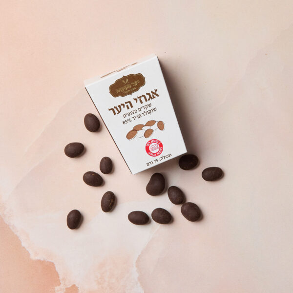 קופסה לבנה עם הכיתוב IMG_2091, ועליה הכיתוב בעברית "85% שוקולד מריר שקד מצופים", מונחת על גבי שיש ורוד ובז' עם שקדים מצופים בשוקולד מפוזרים סביבה.