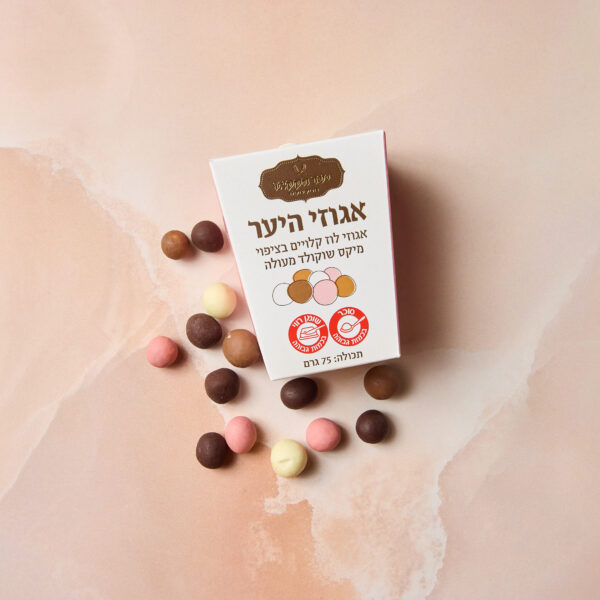 קופסת מצופים לוז מיקס מונחת על שיש ורוד, עם כדורי שוקולד בצבעים חום, לבן וורוד מפוזרים סביבה. על האריזה טקסט בעברית ולוגו עגול בצבע אדום.