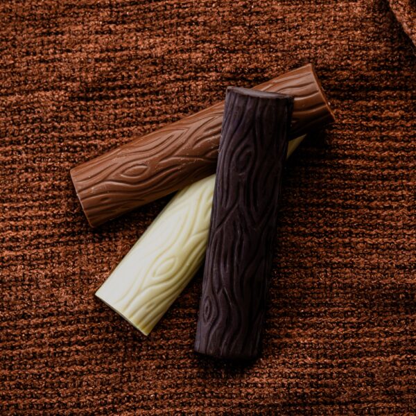 שלושה מקלות שוקולד חלב לוז בעלי טקסטורה - חלב, מריר ולבן - פרוסים על רקע של בד סרוג חום.