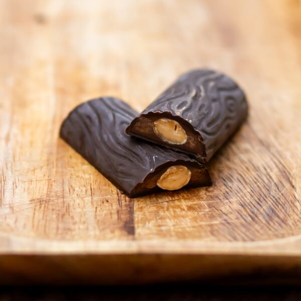 שתי חתיכות של ענף מריר שקדים עם משטח מרקם מוערמות על לוח עץ, כשכל אחת חושפת שקדים שלמים בפנים - פינוק הטבעוני המושלם.