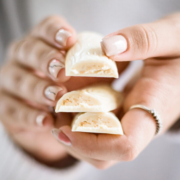 אדם עם ציפורניים מטופחות מחזיק שלוש חתיכות של ענף קוקוס שכל אחת חושפת מילוי במרקם של קוקוס קלוי וקרם שקדים בפנים.