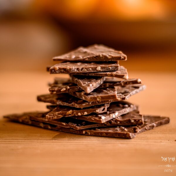 ערימה של חלקי שברים חלל עם אגוזי לוז מונחת על משטח עץ, על רקע מטושטש בגוון חם.