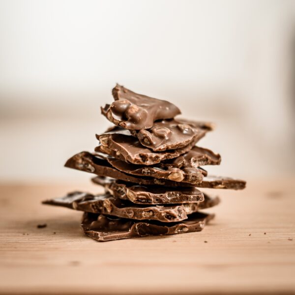 ערימה של שברים חלב פיסטוק לא אחיד עם אגוזים גלויים יושבת על משטח עץ על רקע בהיר מטושטש.