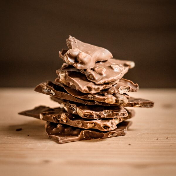 ערימה של שברים חלב קשיו שבורים בצורה לא אחידה יושבת על משטח עץ בהיר על רקע חום מטושטש.