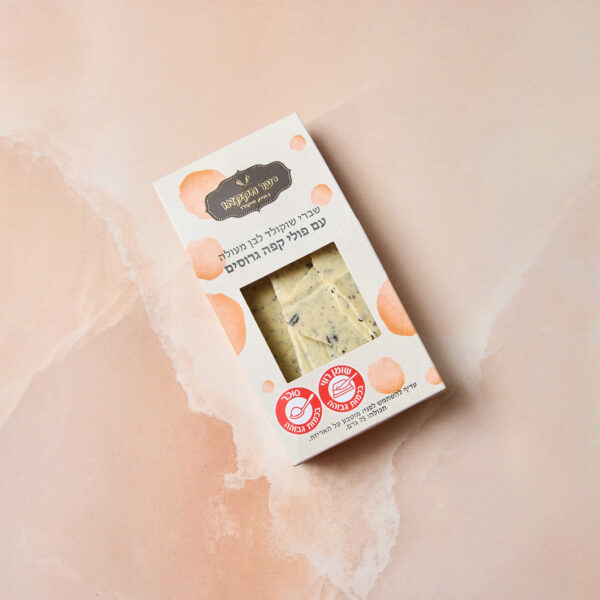 קופסת שוקולד מלבנית עם חתיכות עוגיות, עם טקסט ולוגואים בעברית, המדגישים את המילים "שברים לבן עם קפה", על רקע ורוד בהיר במרקם שיש.