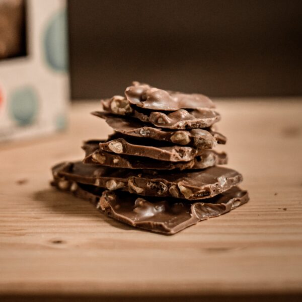 ערימה של שברים מריר שקדים עם שברי שקדים גלויים יושבת על משטח עץ, קופסה מטושטשת ברקע.