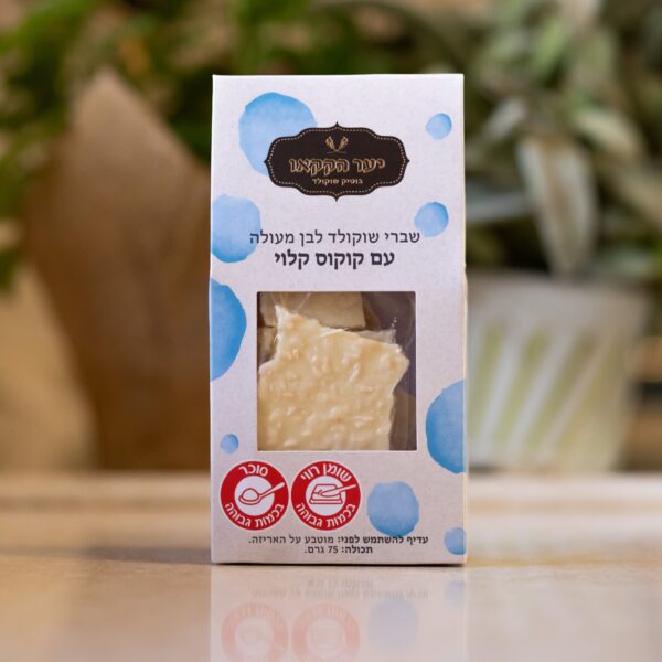 קופסת שברים קוקוס עם אריזת נקודות כחולות וטקסט בעברית, עם תוויות ללא תוספת סוכר, ללא גלוטן וקוקוס קלוי. ברקע ניתן לראות צמח מטושטש.