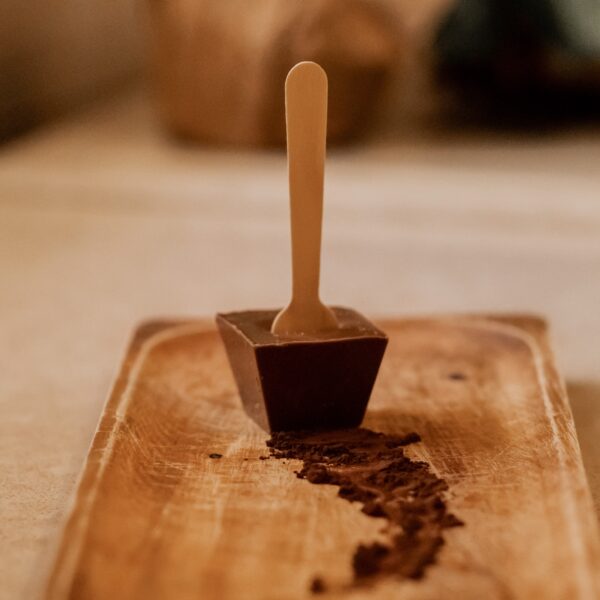 מגש עץ מחזיק גוש של שוקו חלב כשכף עץ זקופה במרכזו, ושובל של אבקת קקאו ואגוזי לוז מוביל הרחק מהשוקולד.