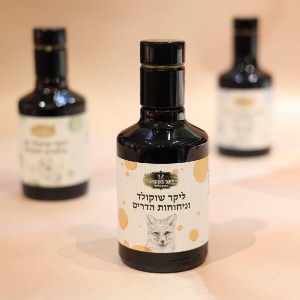 בקבוק כהה קטן המסומן בעברית עם איור פנים של חיה ניצב בולט ורומז על הטעמים העשירים של ליקר הדרים. שני בקבוקים דומים דוהים באלגנטיות אל הרקע על משטח בהיר.