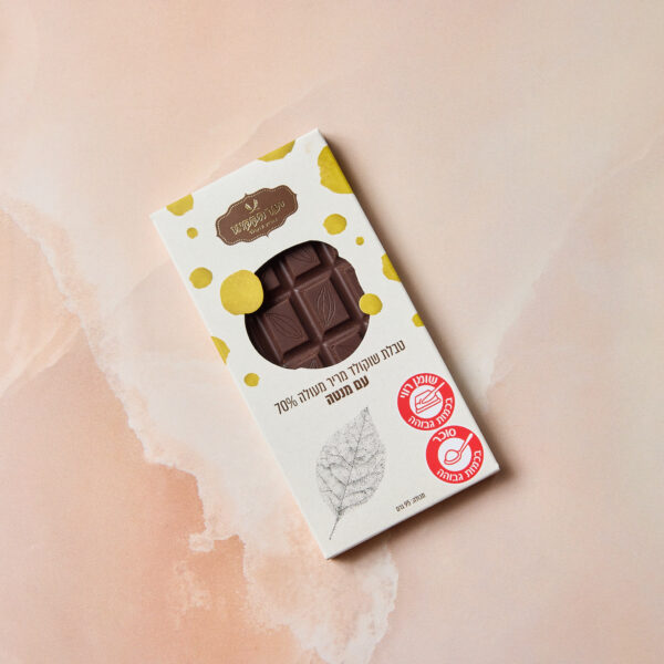 חפיסת שוקולד מלבנית, עם הכיתוב "טבלה מריר מנטה", מונחת באריזה לבנה עם כתמים צהובים, עם טקסט בעברית וסמלי הסמכה אדומים על רקע ורוד בהיר. חלון קטן חושף את השוקולד המפוצל שבפנים.