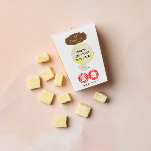 קופסה לבנה עם הכיתוב "IMG_2102" בטקסט עברי וסמלים מונחת על משטח ורוד בהיר, מוקפת בקוביות קטנות מצופות סוכר בצבע צהוב, הדומות לטעפלס שוקולד.
